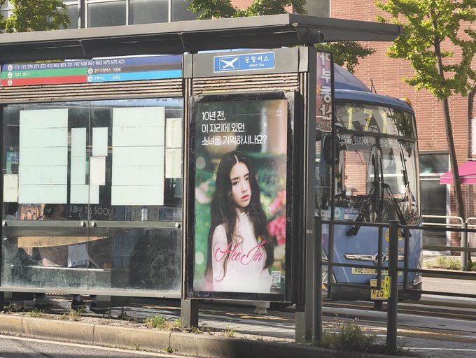 An advertisement at a Korean bus stop features a poster with a young woman and text asking for missing person information, with a blue bus parked nearby.