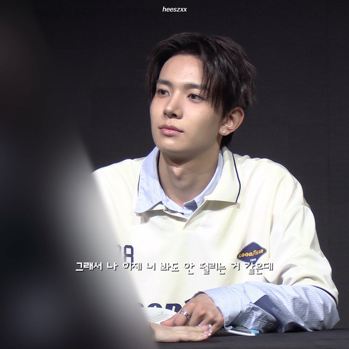 A young man with dark hair wearing a white and blue varsity-style jacket looks off to the side during what appears to be an interview, with Korean subtitles reading 'So there's nothing I can't say in front of you either.'
