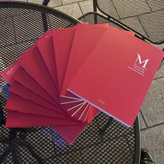 A fan of red menus fanned out on a metal patio table, with the top menu showing a large "M" logo for "Butterfly" restaurant.