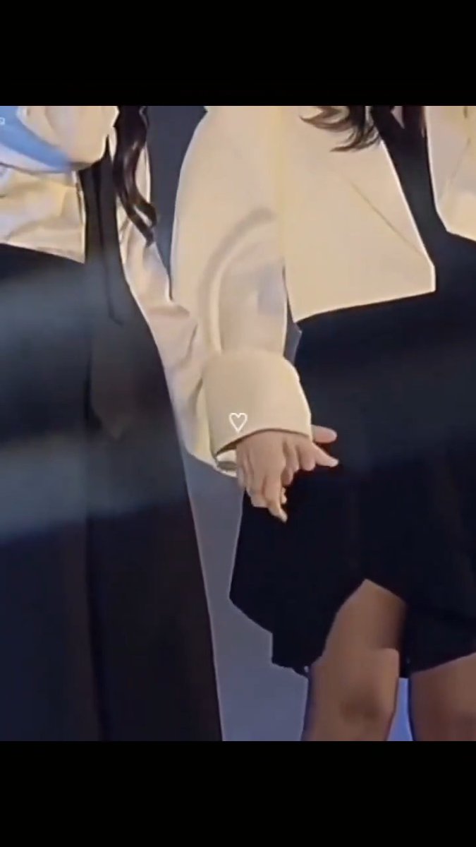 A fan appears to be holding hands with someone wearing a cream-colored jacket, with a small heart emoji overlaid on the image.