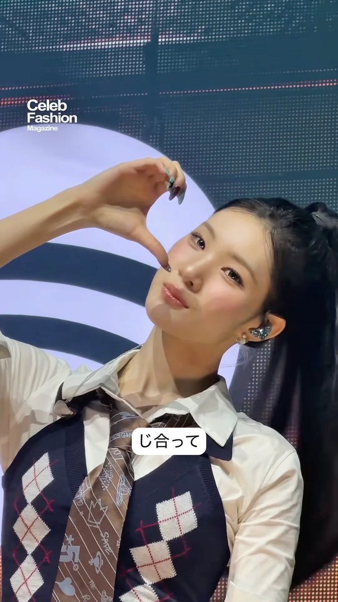 A photo of a young woman making a finger heart gesture, wearing a white shirt with argyle vest and tie, with Japanese text 'じ合って' (matching/fitting) overlaid; 'Celeb Fashion Magazine' watermark is visible.