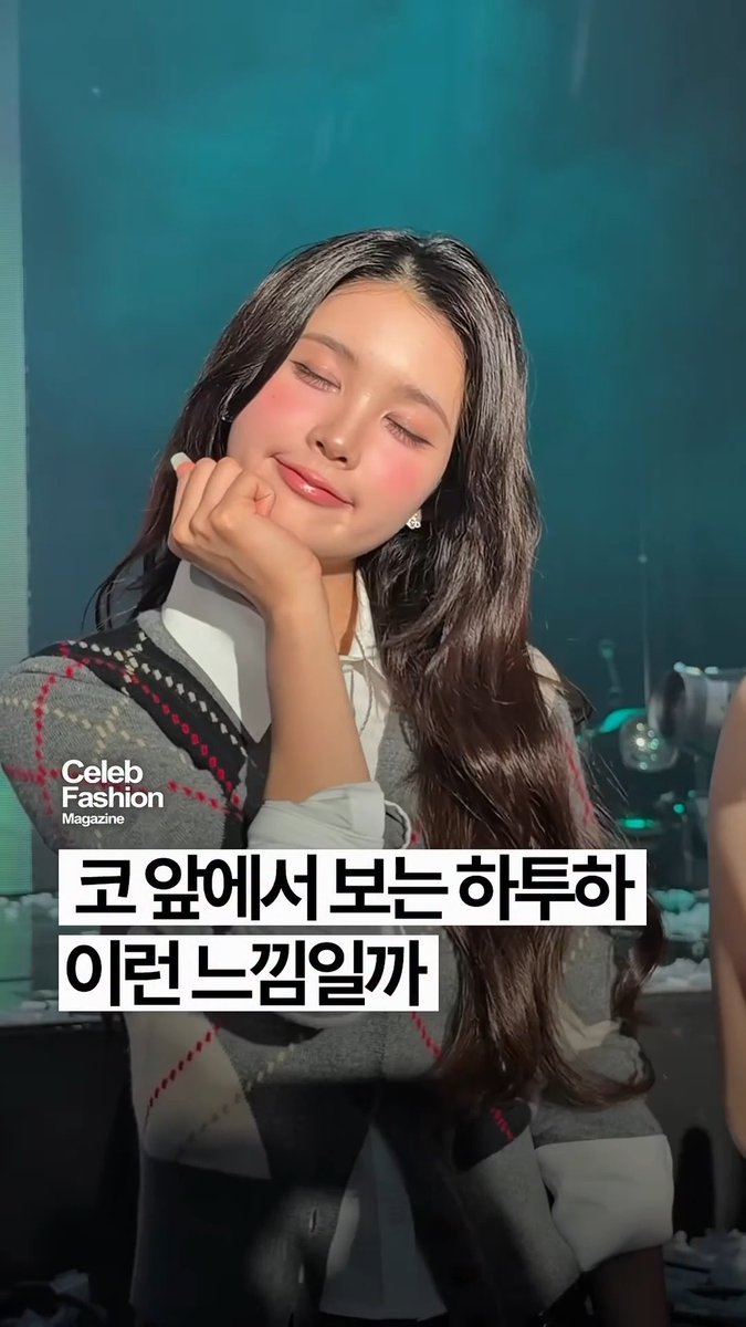 A photo of a smiling woman with long dark hair posing with her hand near her face, wearing an argyle vest over a white shirt, with Korean text '코 앞에서 보는 히루하 이런 느낌일까' overlaid; 'Celeb Fashion Magazine' watermark is visible.
