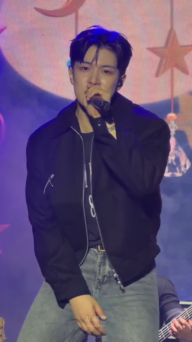 Concert photo of a male performer with dark hair singing into a microphone while wearing a black bomber jacket and gray jeans, with the watermark '구름달 namu#3071' visible.