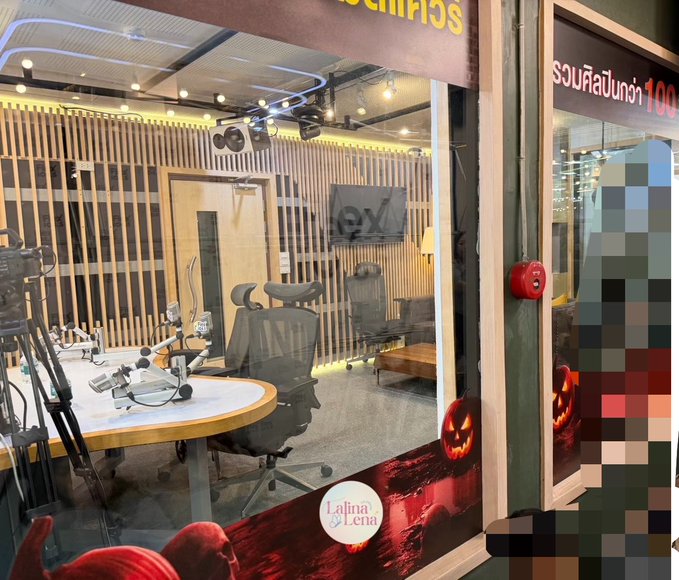 The image shows a radio broadcasting studio decorated for Halloween, with carved pumpkins, a spooky themed window display, and studio equipment including microphones and office chairs visible through the glass. A sign on the right reads "รวมทั้งสิ้นกว่า 100" (totaling over 100), and the "Lalina by Lena" logo appears in the window, connecting to the post about LENA MIU visiting Flex 104.5 radio station for a Halloween-themed appearance.
