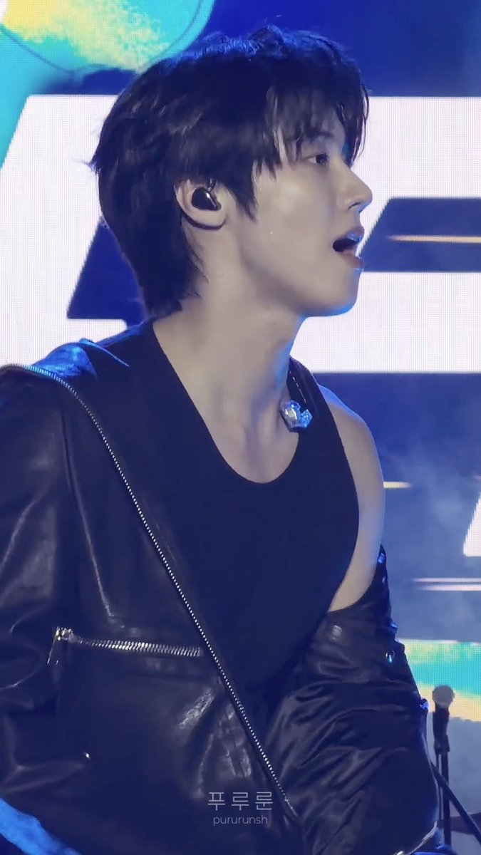 A profile shot captures a young male performer with dark hair on stage wearing a black sleeveless top and in-ear monitors, with a watermark '푸르른sh / pururunsn' visible.