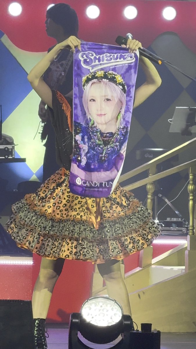 A performer on stage holds up a purple banner featuring an image of a character named 'Shizuku' and the logo 'CANDY FUN'.