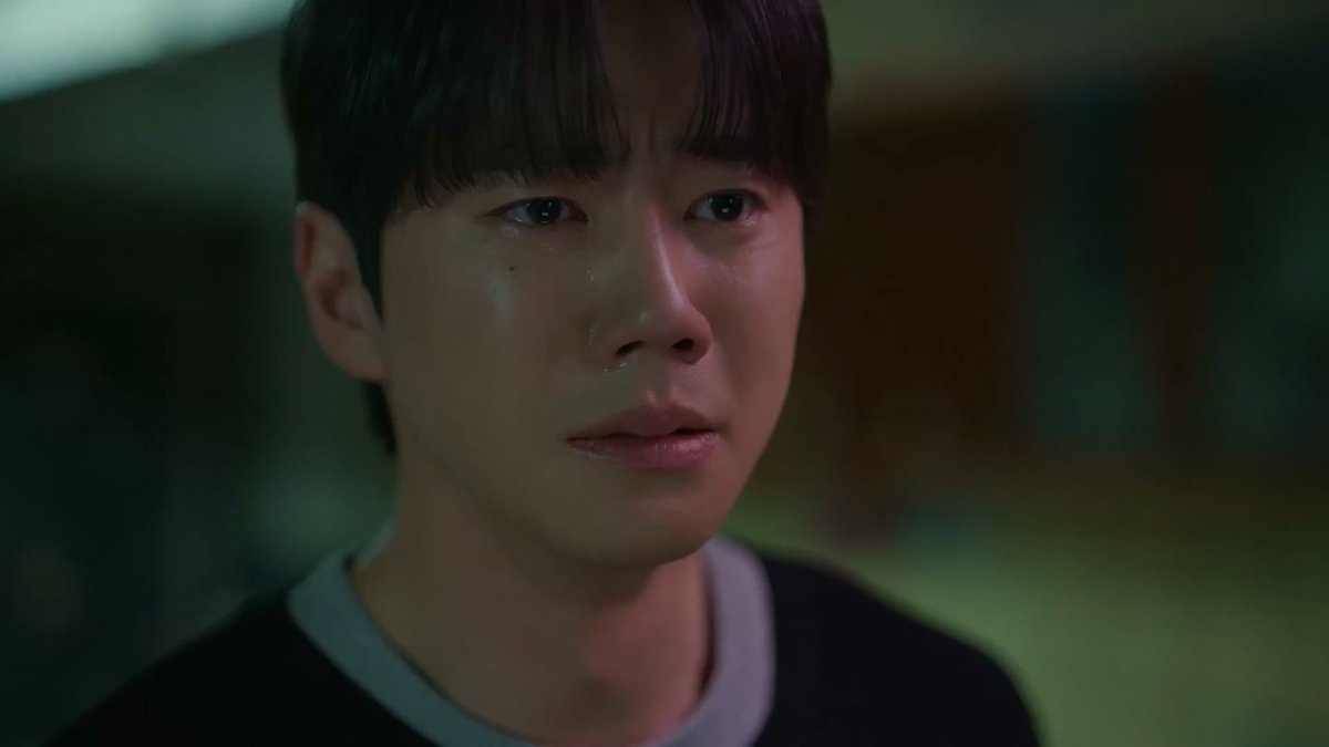 A close-up shot of a young man with dark hair appearing tearful and emotional, seemingly a still from a Korean drama.