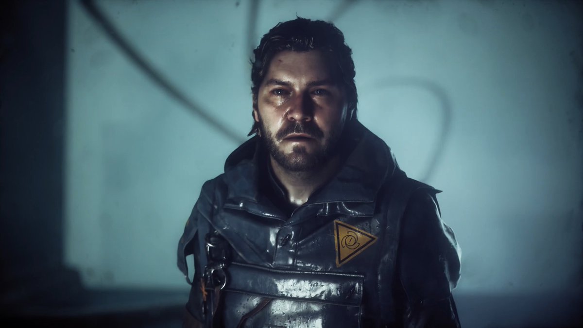 The bearded protagonist, wearing a dark jacket emblazoned with an orange triangular insignia, stares intensely from within a dim, shadowy chamber—an apt visual representation of the post's tagline, capturing the mysterious, reality-warping atmosphere central to the experience of *CONTROL*.
