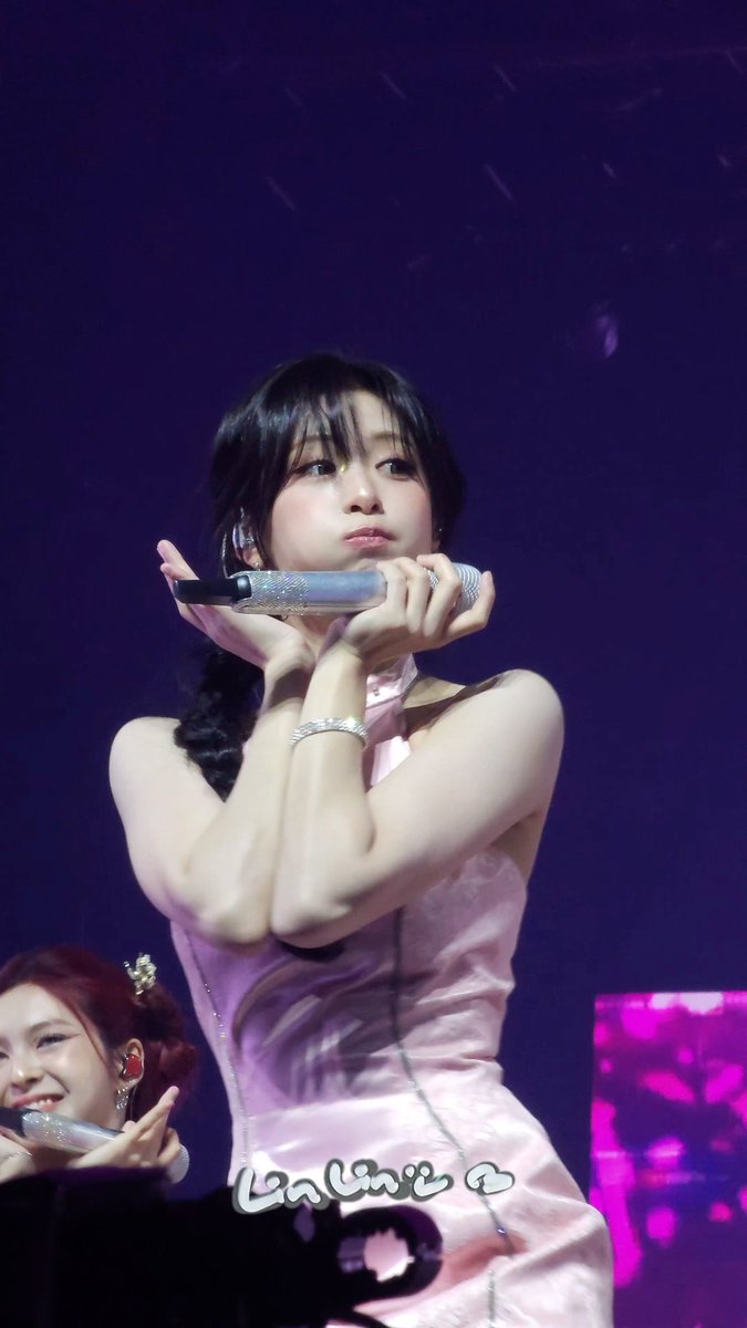 A young woman in a pink dress holds a silver microphone and makes a heart gesture on stage; the name 'Lalune' is written at the bottom.