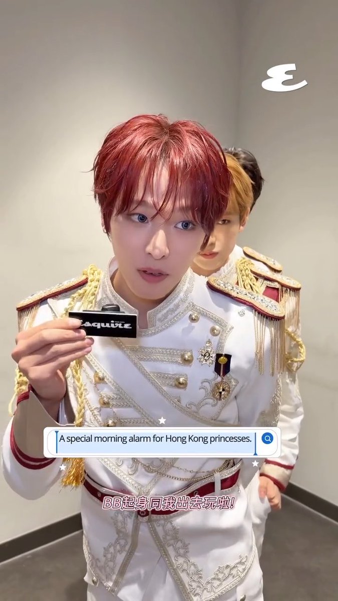 A young man with red hair wearing an ornate white military-style jacket with gold trim holds up a name tag reading 'ZEROBASEONE', with text overlay saying 'A special morning alarm for Hong Kong princesses' and 'BB起身同我出去玩啦!'