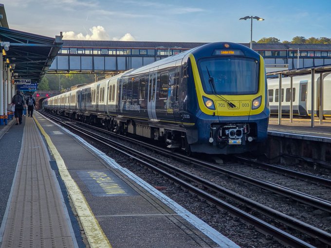 A modern blue and yellow passenger train numbered '701 005' is stopped at a station platform with the word 'KEEP' visible on the ground.