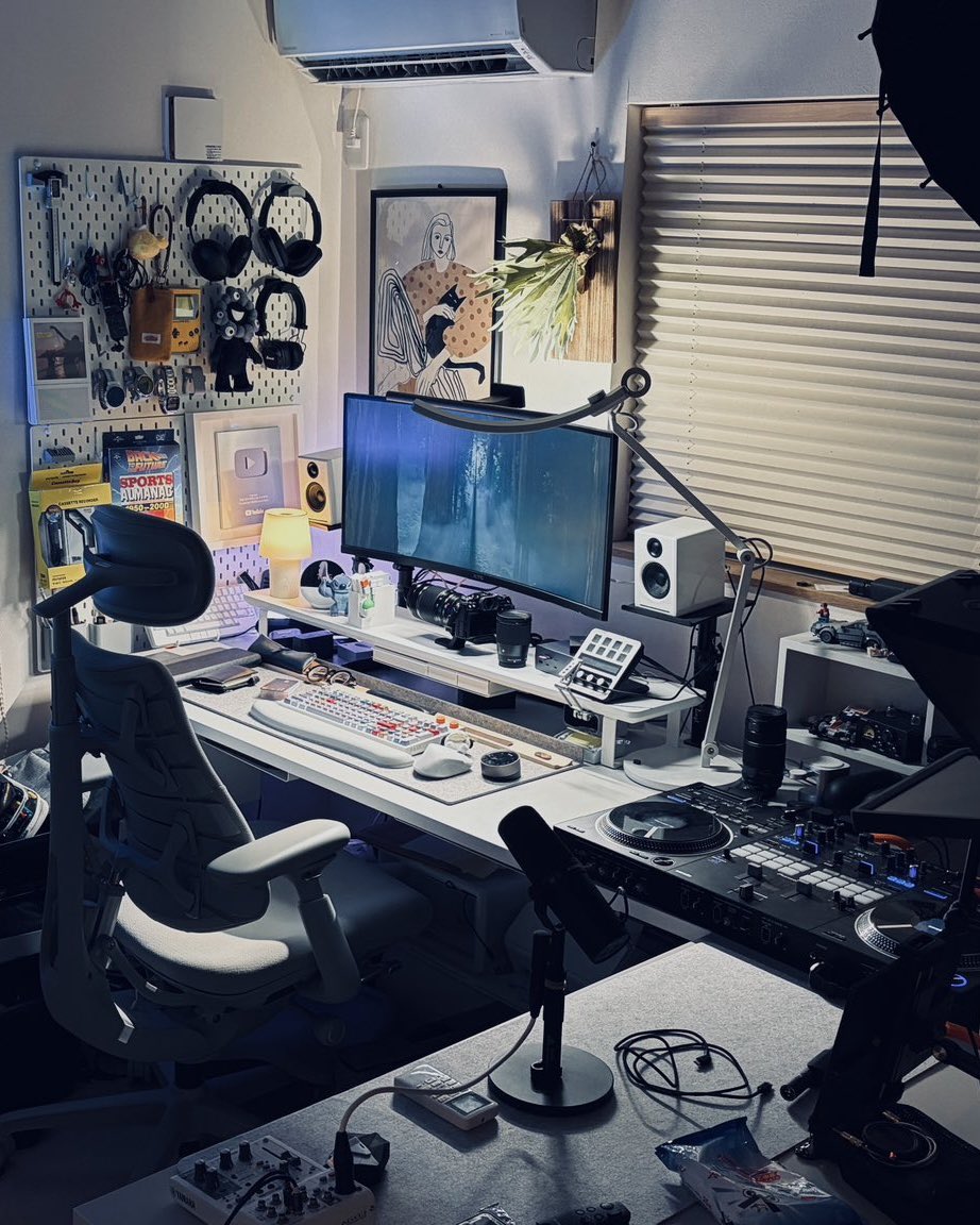 preducts_inc's tweet photo. USER SETUP | PREDUCTS DESK - POLAR

ホワイトとライトグレーでライトトーンな印象のデスク「PREDUCTS DESK - POLAR」。今回はPOLARを愛用いただいている、YouTubeチャンネル「THE オトウサンノヒミツキチ」を運営する @dadsecretbase さんのデスクをご紹介します。

動画制作にとどまらず、ものづくりや他社との仕事まで、日々の制作活動をこの環境で進めているKeiさん。6畳の和室にYouTubeスタジオを兼ねたワークスペースを構え、「秘密基地感」をテーマに、デジタルとアナログが混在したワクワクする仕事環境をつくることを大切にされています。

デスクは作業用と撮影用の2台をL字に配置。作業のしやすさに加え、限られた空間でも動画の絵づくりができるようにという意図があるそうです。

作業用のデスクにはデスクマットを敷き、キーボードやマウスといった入力デバイスに加え、ノートやペン、メガネなど使用頻度の高い小物を手の届く位置に配置しています。

収納は天板裏とDASHBOARDに集約。天板裏にはTray for DESKを、DASHBOARDにはSystem Tray forとRig Gadget Armを取り付け、カメラやStream Deck、SSDなどもDASHBOARD上に常駐。点在しがちな機材を天板裏とDASHBOARDに振り分け、賑やかさはそのままに使い勝手を確保しています。

撮影用のデスクには、マイクやミキサーなど配信・収録に関わる機材に加え、DJコントローラーも並びます。

そして、この部屋で数年をかけて試行錯誤を重ねてきたのがライティング。撮影用の大型照明に加え、デスクにはBluetoothで色を変えられるテープライトを貼り、パソコンの背面や窓際にはPhilips HueのLEDを配置。背景には無印良品のライトやBenQの卓上ライトも組み合わせています。

LEDの色をガジェット感の強いトーンに振り切る。POLARのシンプルな色味が、そのLEDの色を素直に受け止めてくれるといいます。

ガジェット類が並ぶ有孔ボード、壁に掛けたギター、「バック・トゥ・ザ・フューチャー」のデロリアンモデル。実用と"好き"が入り混じっているのが、この空間の持ち味です。