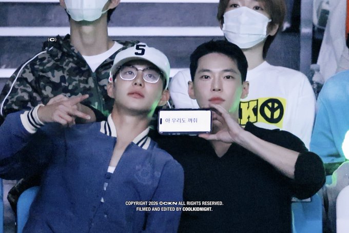Two men wearing masks, one with a white 'S' cap and glasses and one in a black shirt holding up a phone displaying Korean text '아우라도 캐치', credited at the bottom 'COPYRIGHT 2026 C-OKN ALL RIGHTS RESERVED. FILMED AND EDITED BY COOLKIDNIGHT.'