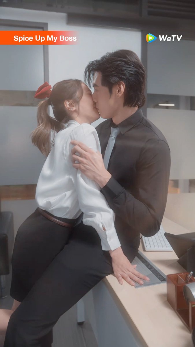 A promotional poster for the WeTV series "Spice Up My Boss" shows a man and woman sharing a passionate kiss in an office setting, with the woman perched on a desk. The image features the show's title "Spice Up My Boss" in the top left and the WeTV logo in the top right, visually aligning with the Thai post announcing the show's daily 6:00 PM airing exclusively on WeTV.