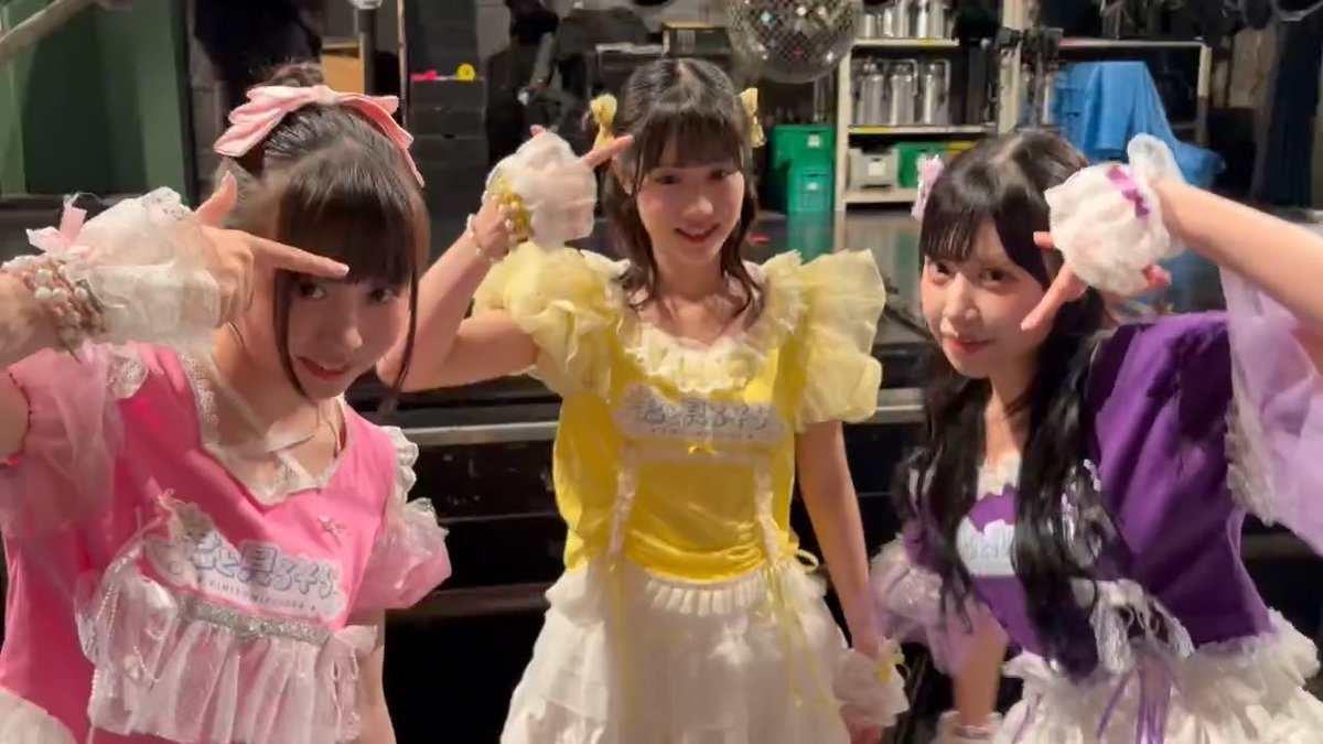 Three young performers in frilly pink, yellow, and purple maid-style costumes pose together backstage, flashing peace signs with Japanese text "きみそら" (KimiSora) visible on their outfits. The image captures an off-shot moment that complements the post about KimiSora's "Lemon Boy Championship" sequel.