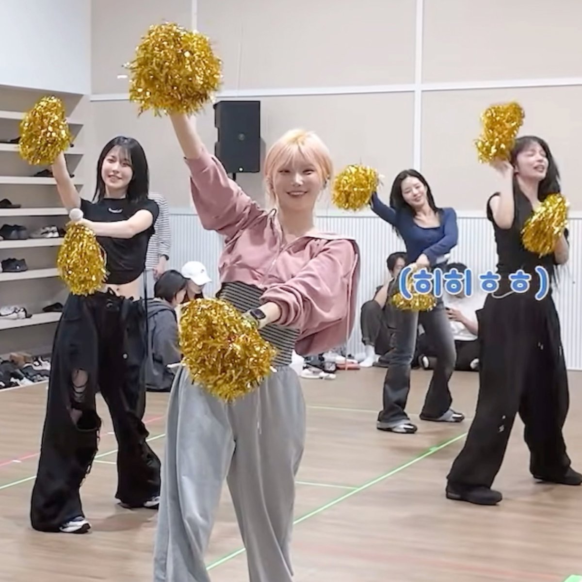 A group of young women dance in a studio holding gold pom-poms, with Korean text "(히히히)" overlaid on the right side.