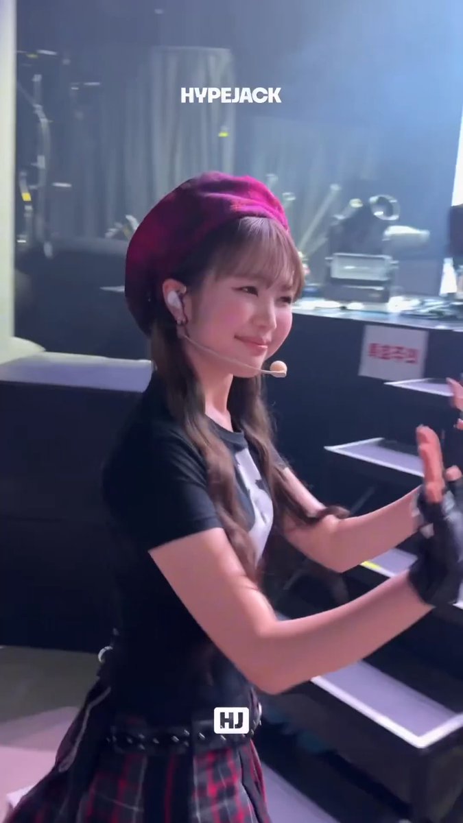 A young woman with long brown hair wearing a red beret and headset microphone performs on stage, with the watermark 'HYPEJACK' and 'HJ' visible.