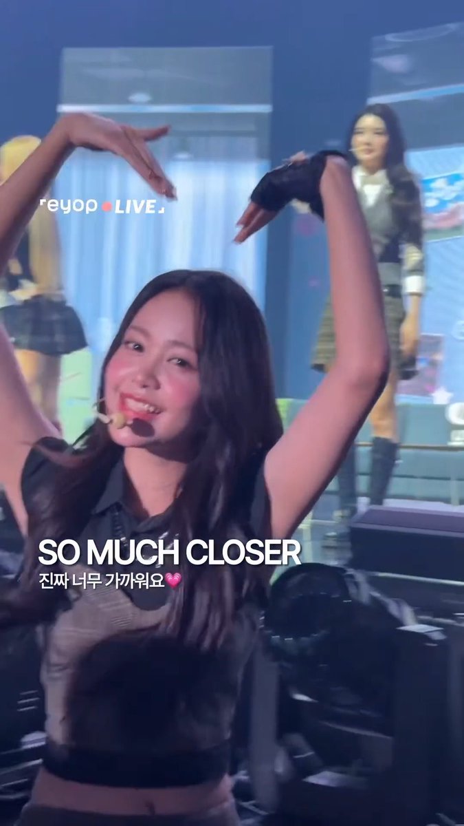 A concert scene featuring a smiling young woman with long dark hair raising her arms in the air, wearing a black glove, with text overlays reading 'reyop LIVE', 'SO MUCH CLOSER', and '진짜 너무 가까워요' (with a heart symbol).