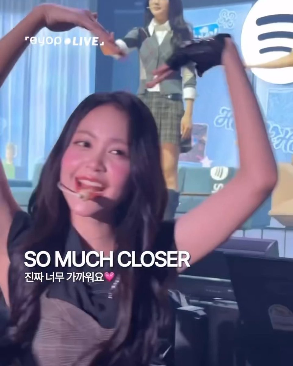 A screenshot from a K-pop live broadcast featuring a smiling female idol making a heart shape with her arms, with the overlaid text 'SO MUCH CLOSER' and a Korean caption.
