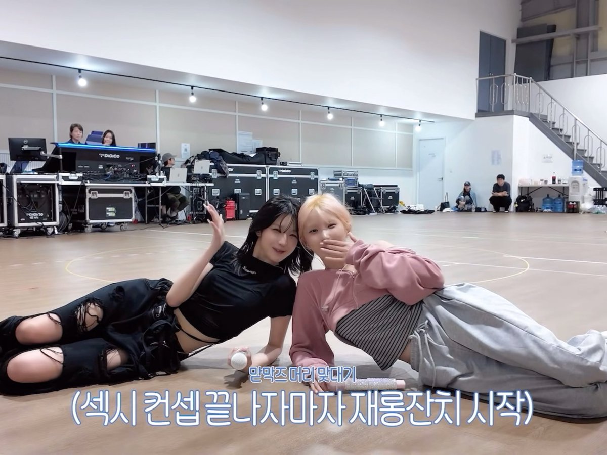 Two K-pop idols lying on a practice room floor with Korean text overlay reading '맘먹즈 머리 맞대기 (섹시 컨셉 끝나자마자 지름집친 시작)'.