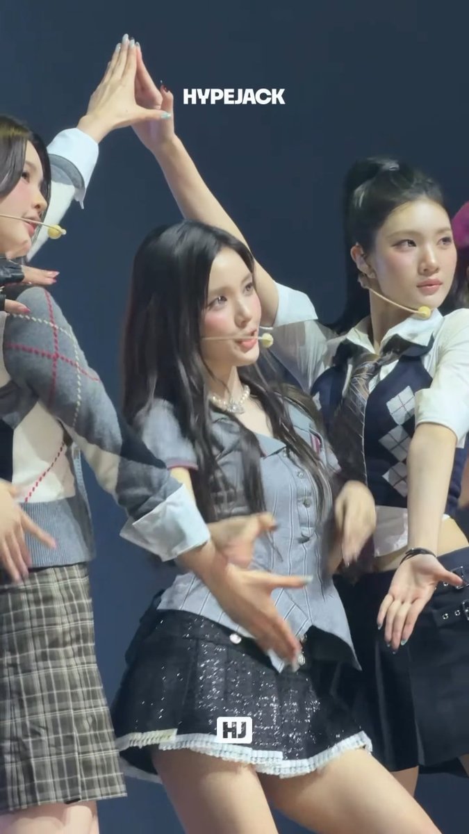 A performance photo of three K-pop female idols on stage in coordinated schoolgirl-inspired outfits, with the central figure dancing and 'HYPEJACK' watermarked at the top.