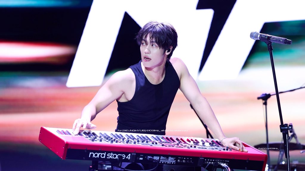 A young male musician performs on stage, playing a red "nord stage 4" keyboard while wearing a black tank top and in-ear monitors, with a microphone stand positioned beside him. The watermark "for [BEUNG-MYE] SIOGH-L" is visible, and the caption humorously comments on the camera angle and his "Vita Synth mod sound" performance.