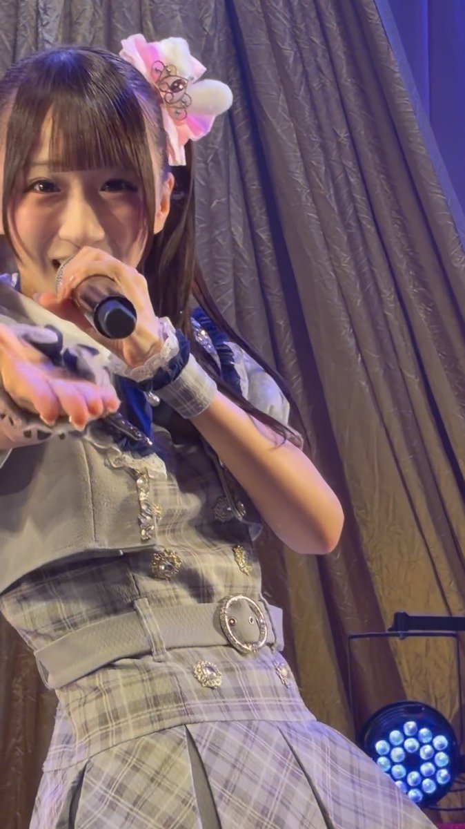 A young performer with brown hair adorned with a pink and white bow holds a microphone close to her mouth while wearing a plaid gray outfit with a decorative belt and floral embellishments, standing before a gold curtain and blue stage lighting.

The "だいすきだよ" (meaning "I love you so much" in Japanese) caption reflects the warm, affectionate sentiment of the fan moment captured during what appears to be an idol performance.