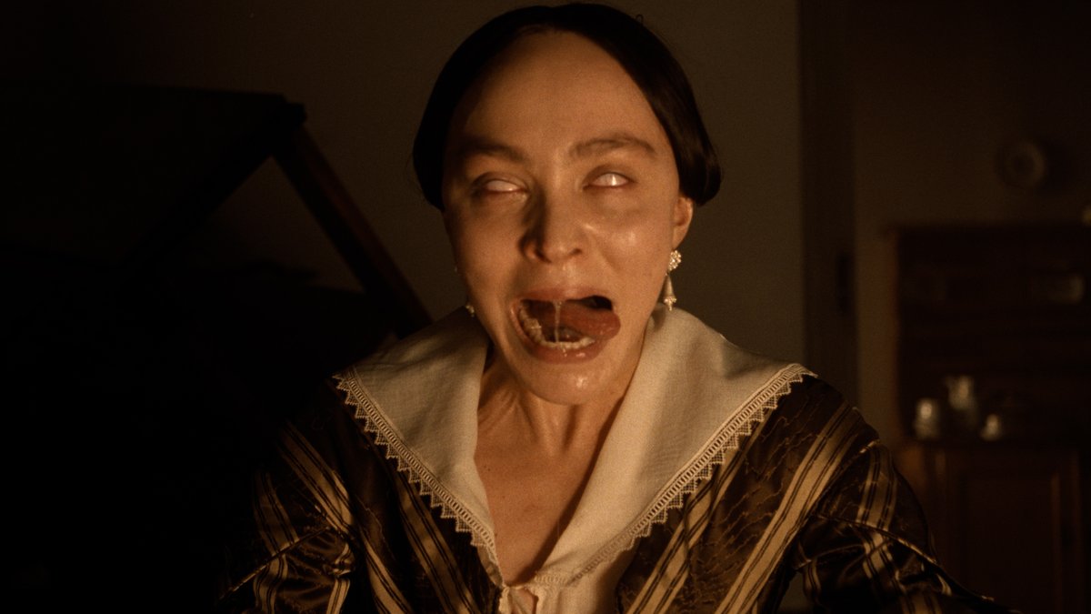 A woman with dark hair parted down the middle, wearing a period dress with a high lace collar and gold earrings, is shown with her eyes rolled back and mouth agape in a haunting, unsettling expression—capturing the eerie horror atmosphere of Lily-Rose Depp's performance in Nosferatu.