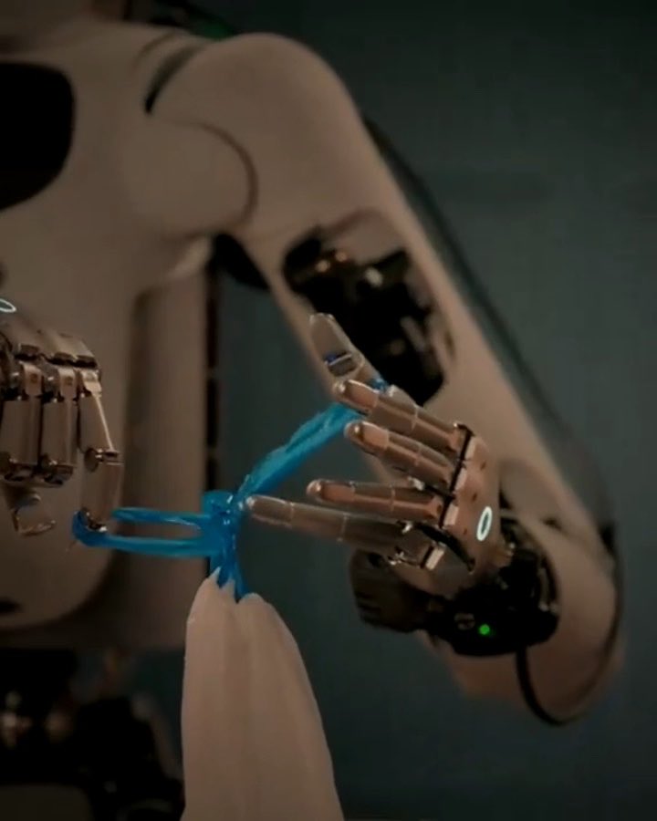 A close-up image of a robotic hand with white and metallic fingers manipulating a bright blue string or plastic material, showing advanced robotic dexterity with a green indicator light visible.