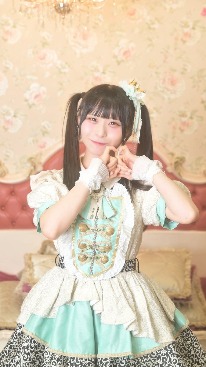 A smiling young woman with long dark hair in pigtails adorned with a bow poses with her hands forming a heart shape near her face, wearing an elaborate pale green and cream lolita-style dress with gold and pearl detailing. The image captures Hanasaki Himi in costume, matching the TikTok post promoting her "God, Don't End the Summer" dance performance (#マリクラ).