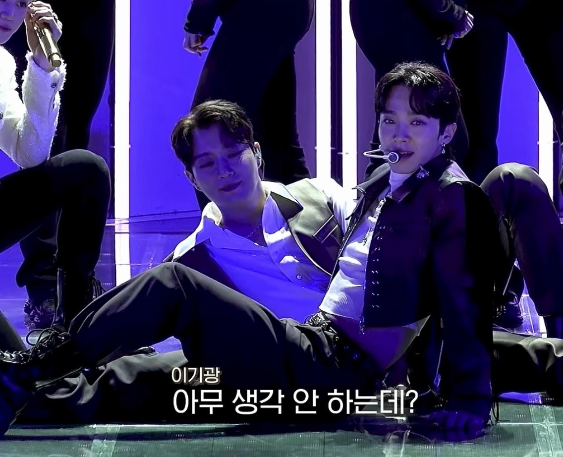 K-pop performers from Lee Gi-gwang (이기광) on stage in dark outfits, with Korean subtitles asking '아무 생각 안 하는데?' (I'm not thinking anything?).