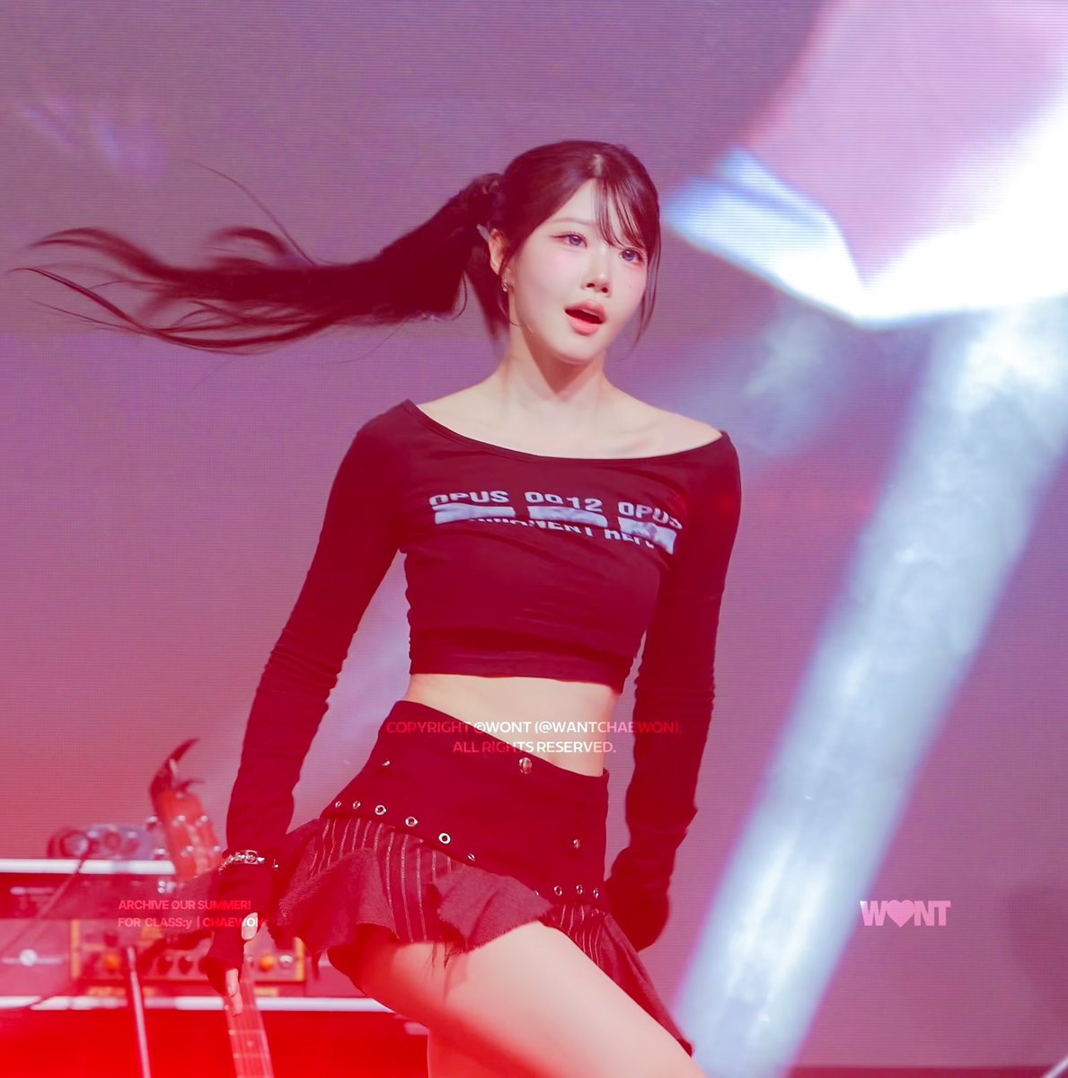 A female performer on stage wearing a black long-sleeve off-shoulder crop top with 'OPUS 0012 OPUS' text and a black pleated skirt, with watermarks reading 'COPYRIGHT ©WON1 (@WANTCHAEWON). ALL RIGHTS RESERVED.', 'ARCHIVE OUR SUMMER! FOR CLASS:y | CHAEWON', and 'WON1'.