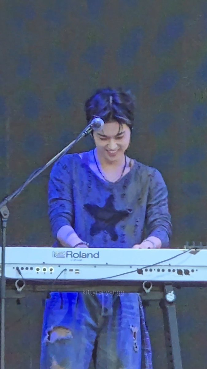 A performer with dark hair smiles while playing a Roland keyboard on a blue-lit stage, with the watermark "kittyranyangg" visible.