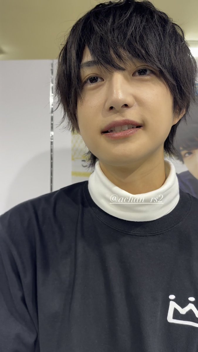 A young man with dark, shaggy hair wears a black sweatshirt with a white crown logo over a white turtleneck, with the watermark '@achan_rs2' visible across his chest.