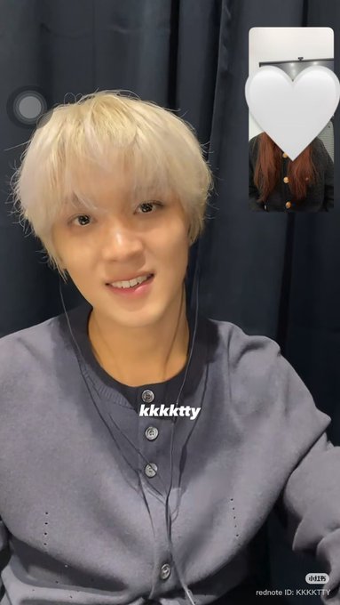 The image shows a young man with platinum blonde hair smiling during what appears to be a video call, wearing a blue henley shirt with earbuds in. The text "kkkktty" is visible on the image, along with a rednote ID of "KKKKTTY," and a small heart-shaped inset in the top right corner. This corresponds to the post about Haechan from NCT at the NY Music Yeongtong Fan Sign event on October 2, 2026.