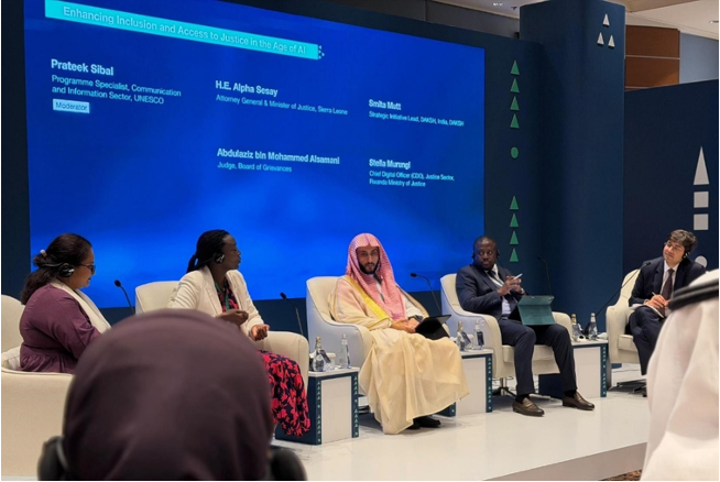 A panel discussion titled 'Enhancing Inclusion and Access to Justice in the Age of AI' features individuals seated on a stage, including speakers Prateek Sibal, H.E. Alpha Sesay, Sinha Muti, Abdulaziz bin Mohammed Alansari, and Stella Murugi.
