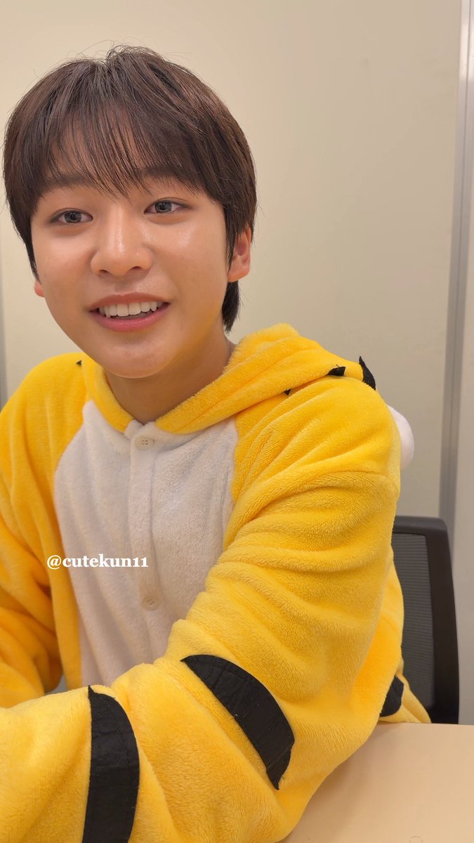 A selfie of a smiling young man wearing a yellow and white tiger-themed onesie, with the text "@cutekun11" visible.