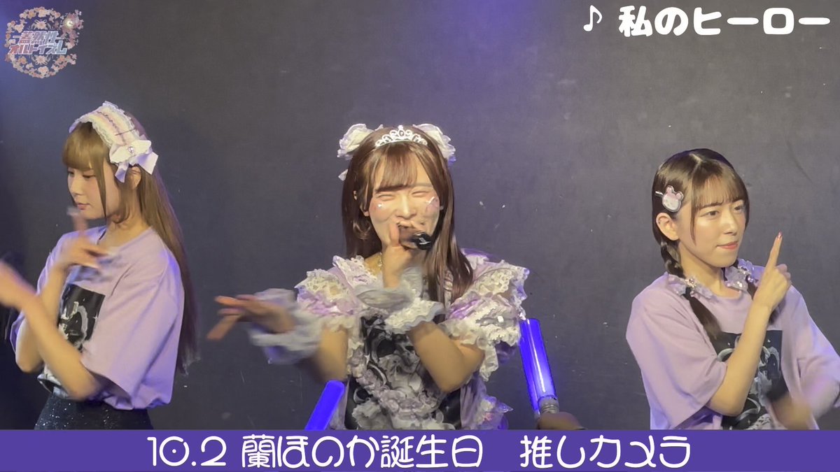 Three Japanese performers on stage in lavender and white frilly maid-style outfits, with text overlays including '♪私のヒーロー' and '10.2 蘭ほのか誕生日 推しカメラ'.