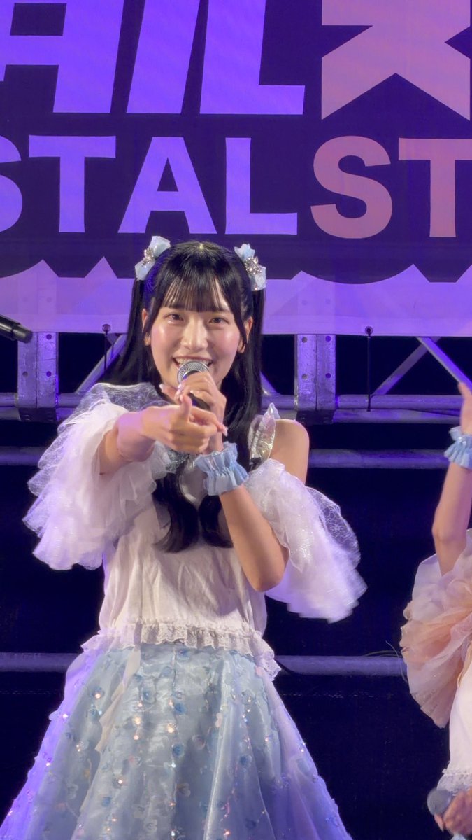 A performer in a blue and white dress with hair bows sings into a microphone on stage, with 'STALST' visible on the backdrop.