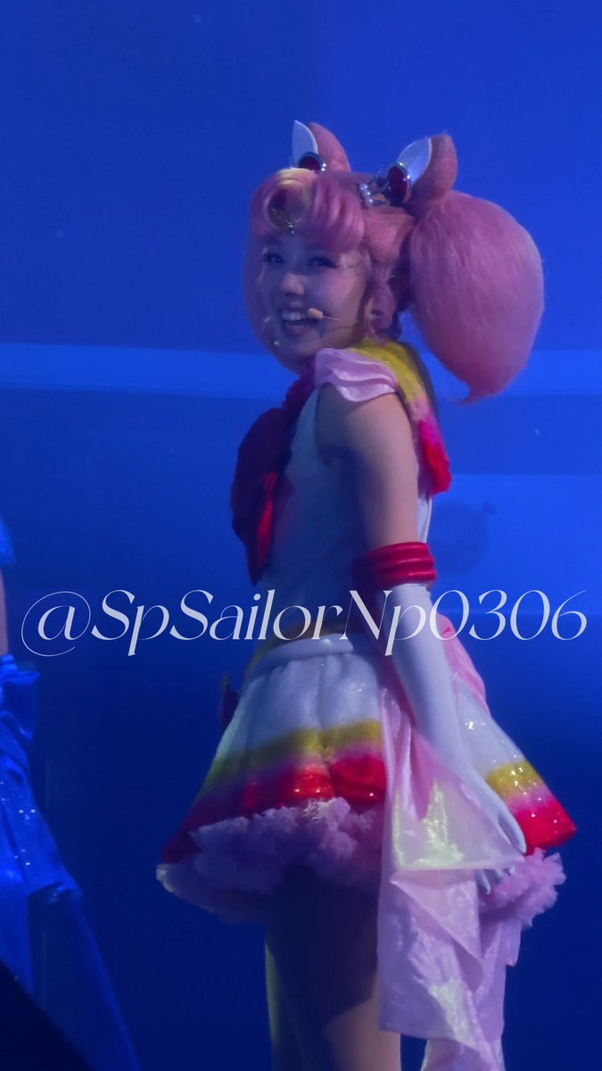 A performer in a pink Sailor Moon-style cosplay costume with pigtails on a blue-lit stage, watermarked '@SpSailorVp0306'.