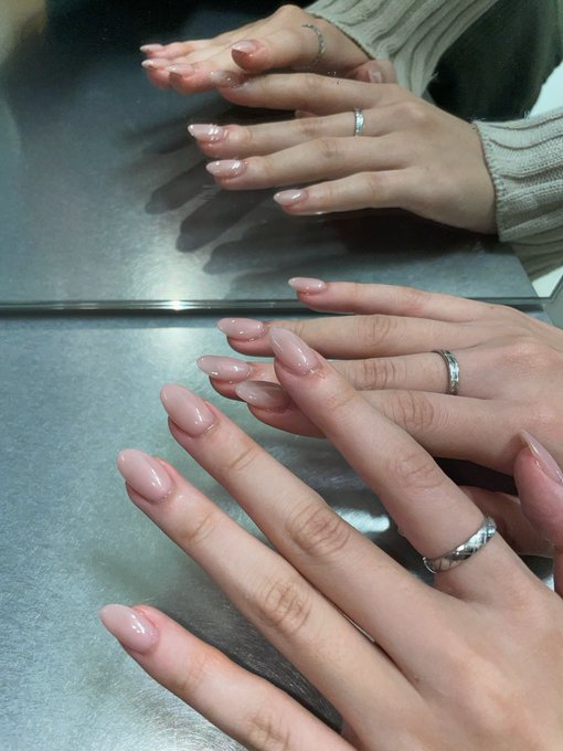 A pair of hands rests on a metal surface, displaying freshly manicured almond-shaped nails with a soft pink nude polish, alongside two silver rings, captured as a photo that was shared on a nail shop's Instagram.