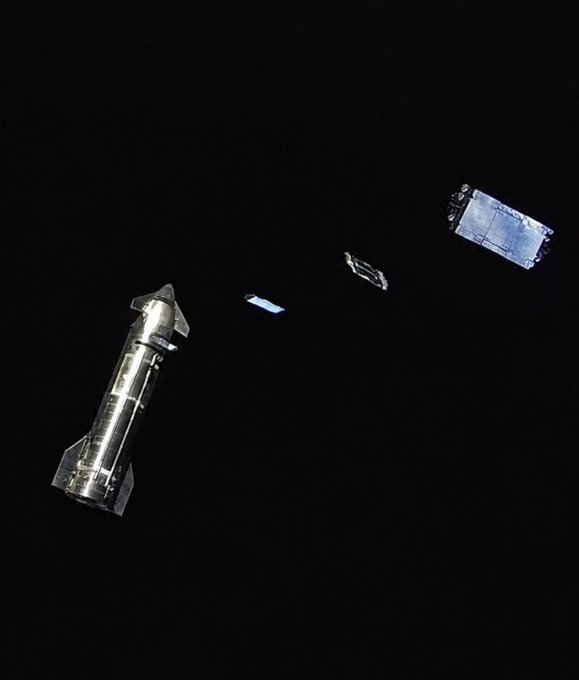 A silver rocket ship floats in the black void of space, separated from several rectangular modules or satellites.