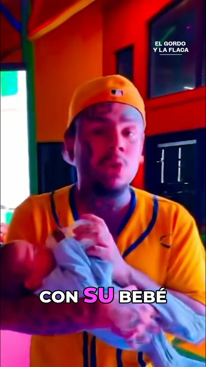 A screenshot from a video featuring a man in a yellow baseball uniform holding a baby, with Spanish text reading 'EL GORDO Y LA FLACA' and 'CON SU BEBÉ' overlaid on the image.