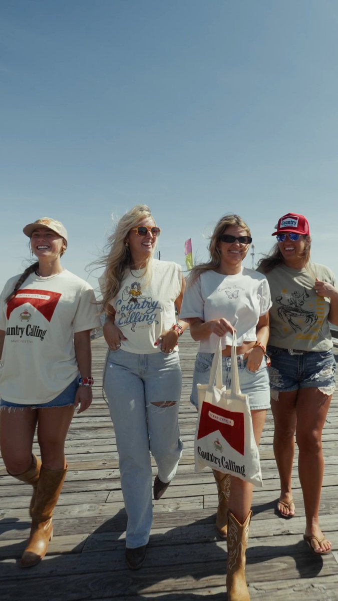 Four young women wearing country/western-themed clothing and 'Country Calling' shirts walking together on a wooden boardwalk.