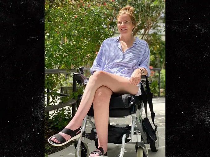 Brooke Eby, an ALS advocate who documented her journey with the disease on social media, sits in a wheelchair outdoors wearing a blue striped shirt and sandals. The ALS Network announced her passing, remembering her as an "extraordinary advocate, storyteller, community builder and friend."
