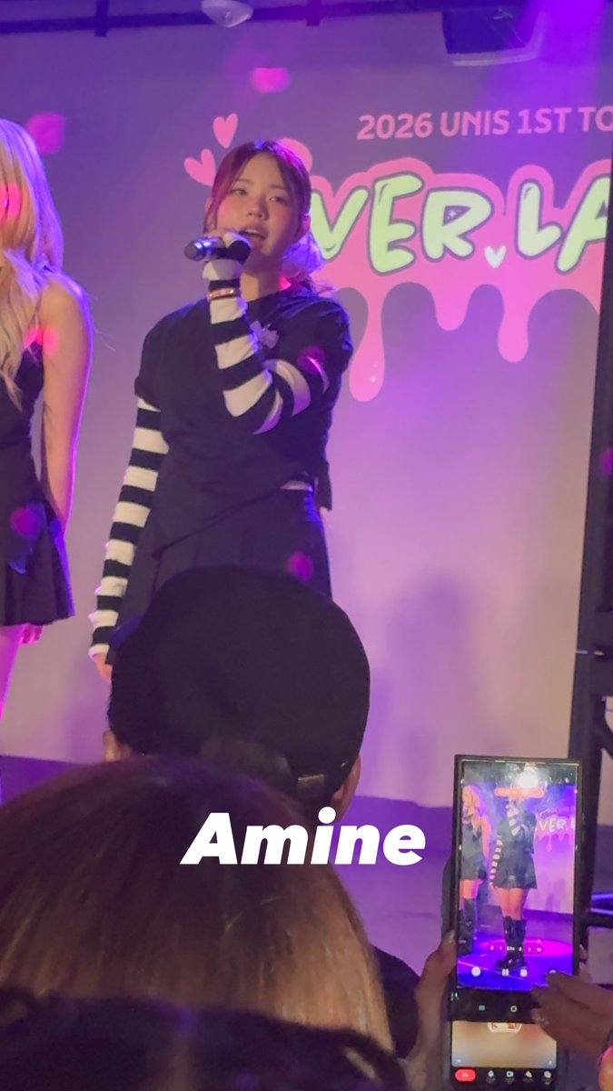 A young woman performs on stage at what appears to be a K-pop concert, with '2026 UNIS 1ST TO...' and 'EVERLA...' visible on the backdrop behind her. The name 'Amine' is written in white text across the bottom of the image.