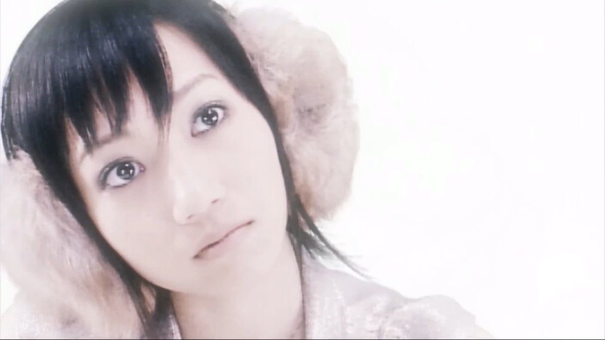 A close-up portrait of a young woman with dark hair and bangs, wearing a furry hat, looking softly at the camera.