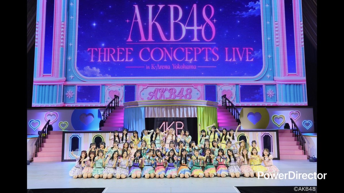 An AKB48 concert photo shows dozens of performers in colorful outfits kneeling on stage with a large screen displaying 'AKB48 THREE CONCEPTS LIVE in K-Arena Yokohama' and 'PowerDirector' watermark visible.