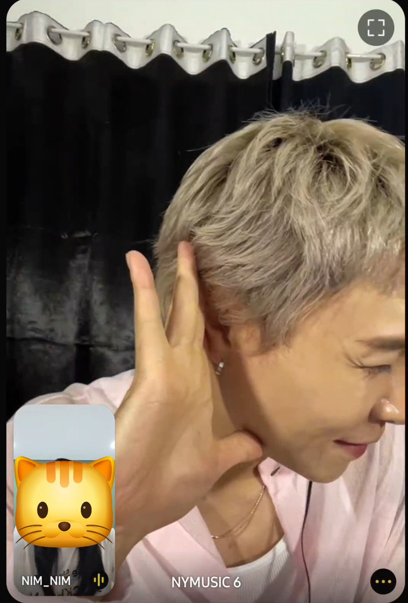 A person with short blonde hair wearing a pink top is seen in a video call or social media interface labeled "NIM_NIM" and "NYMUSIC 6," making a hand gesture near their face.