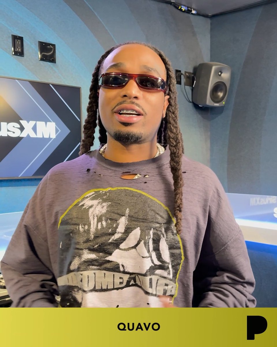 Portrait of rapper Quavo wearing sunglasses and a graphic t-shirt, photographed in what appears to be a SiriusXM studio with his name displayed at the bottom.